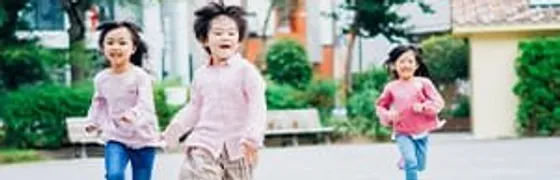 広場で笑顔で走る3人の子どもたち