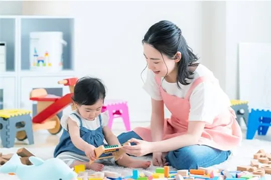 保育士と幼児が積み木で遊ぶ様子