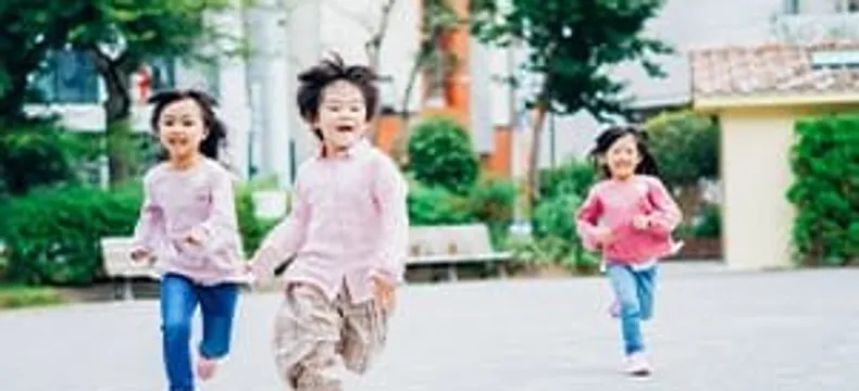 広場を笑顔で走る3人の子ども